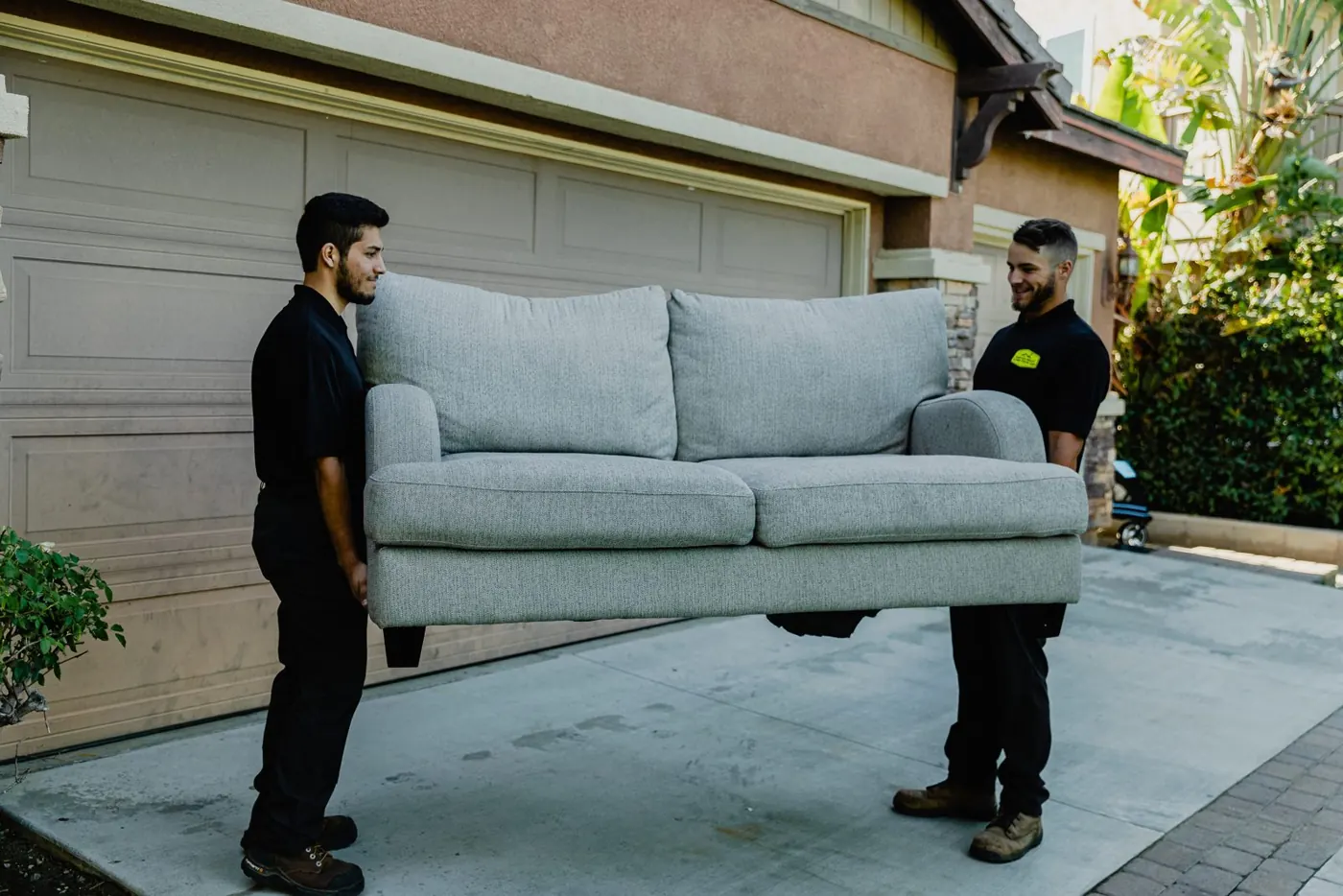 Two team members carrying a couch out of a garage
